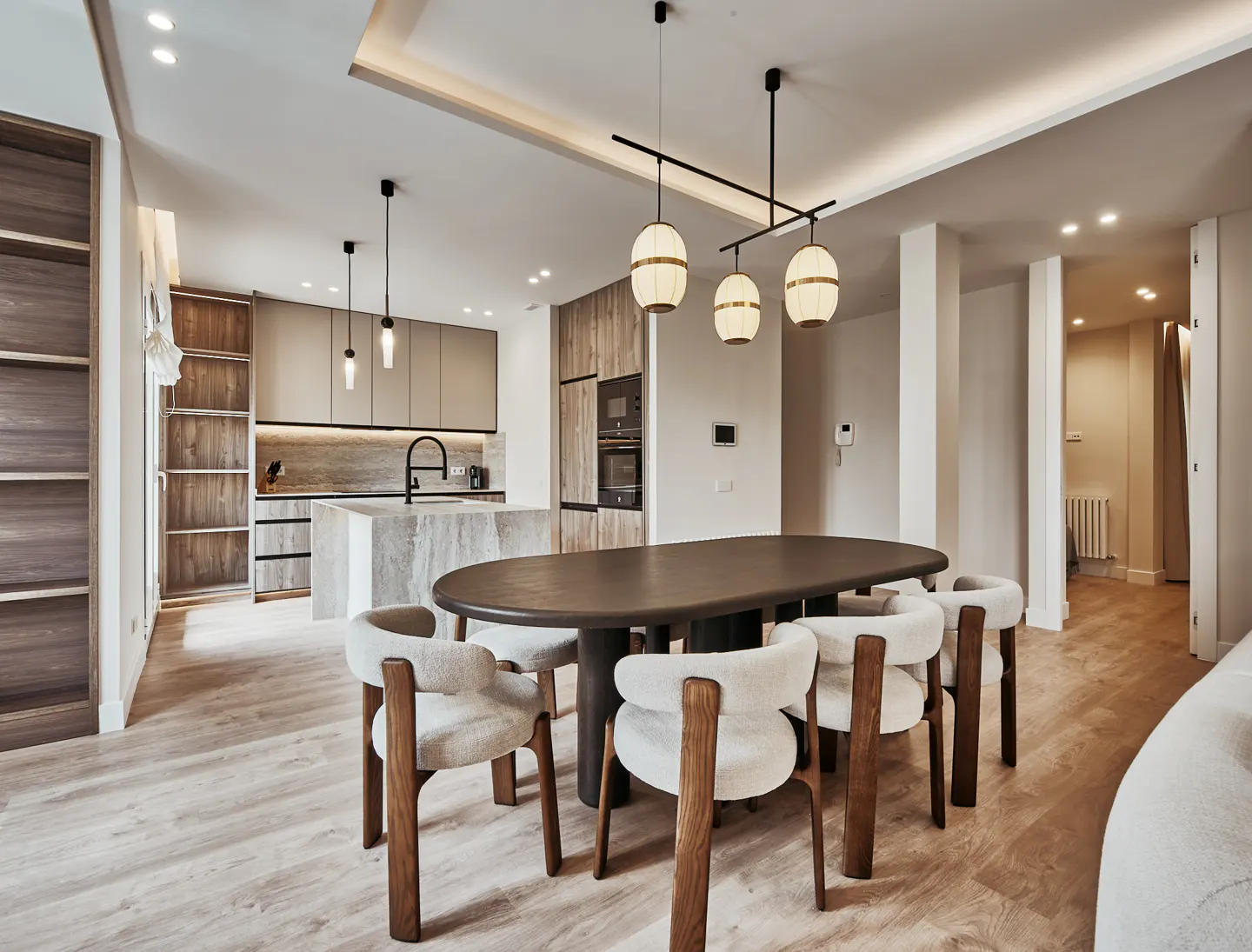 Modern open-plan kitchen and dining area with a dark oval table, cream chairs, and light wood flooring.