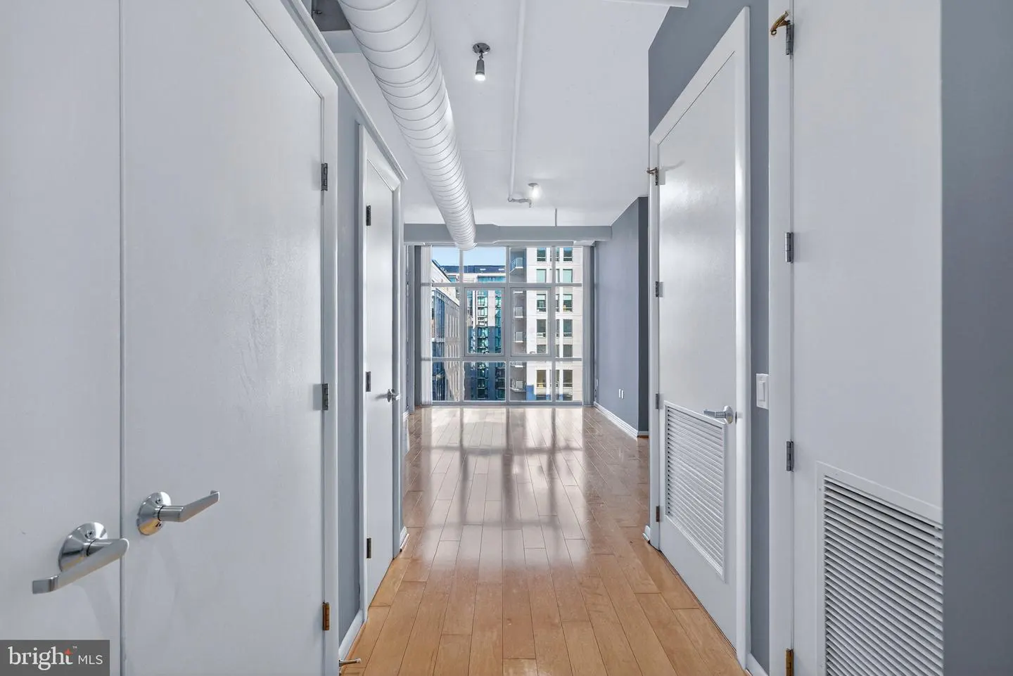 Hallway with light wood floors, white doors, and a large window showing a city view.