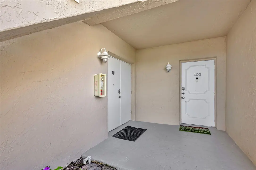 Condo hallway with doors 101 and 102, white doors, beige walls, and gray floor. A fire extinguisher is mounted on the wall.