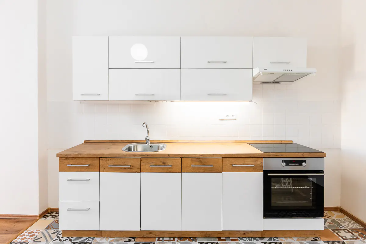 A bright kitchen with white cabinets, wood countertops, a stainless steel sink, and a black oven. The floor has a colorful geometric pattern.