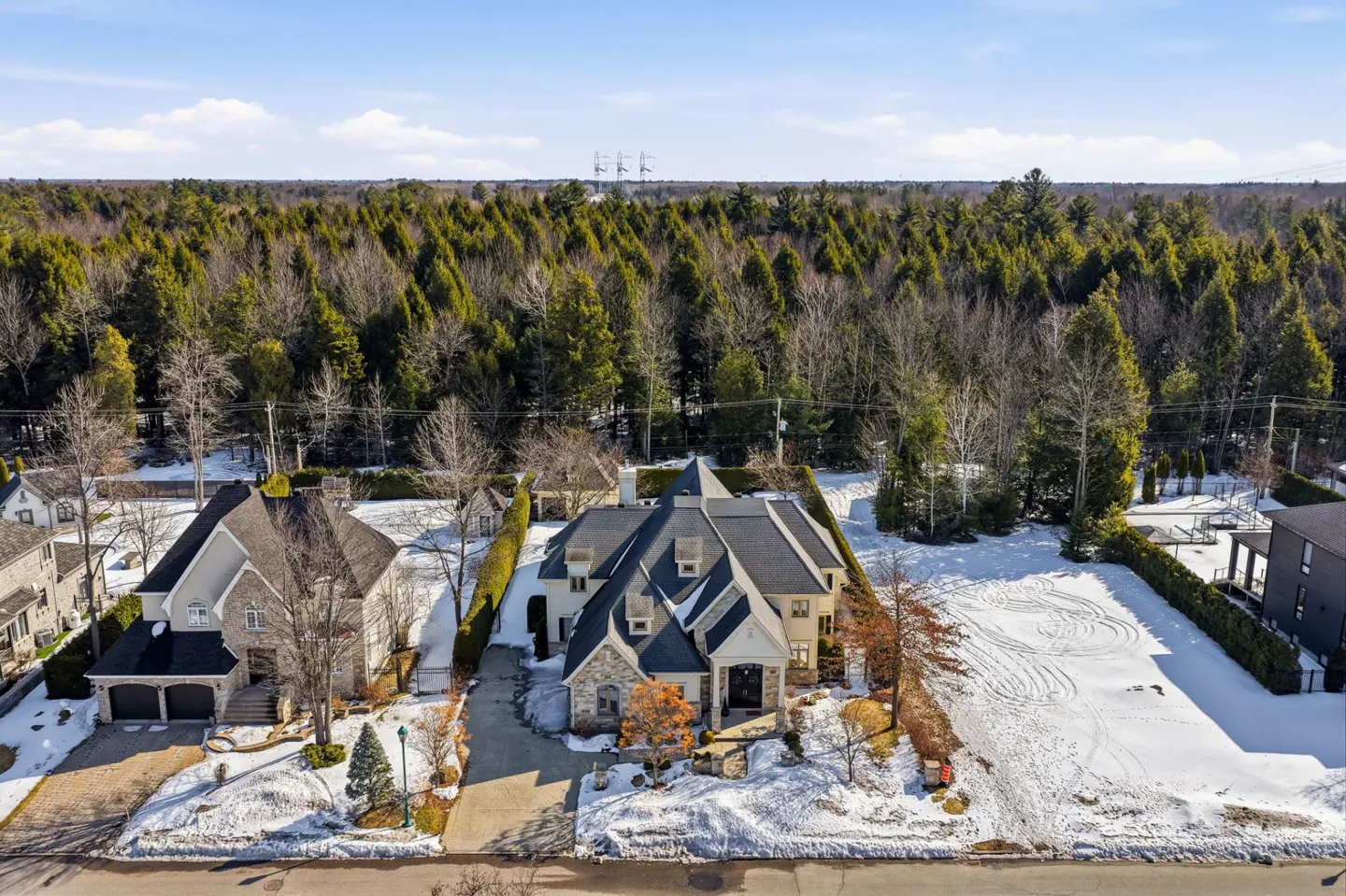 Aerial view of a large, light-colored house with a dark roof, surrounded by snow-covered lawns and trees.