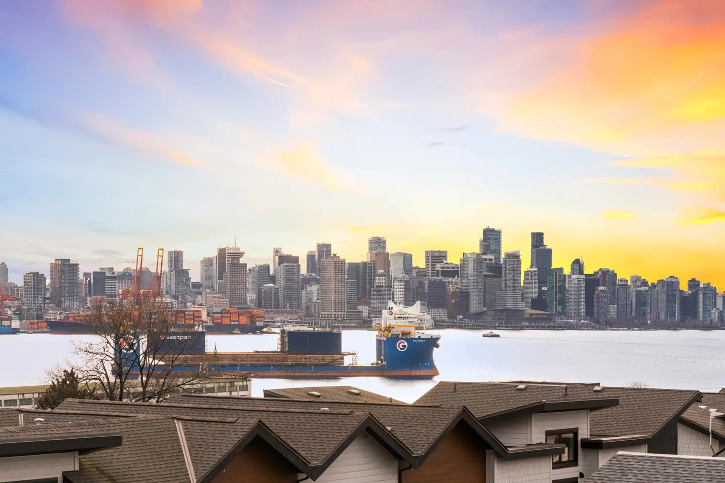 View of Vancouver skyline at sunset from rooftop. Cargo ships sit in the water.