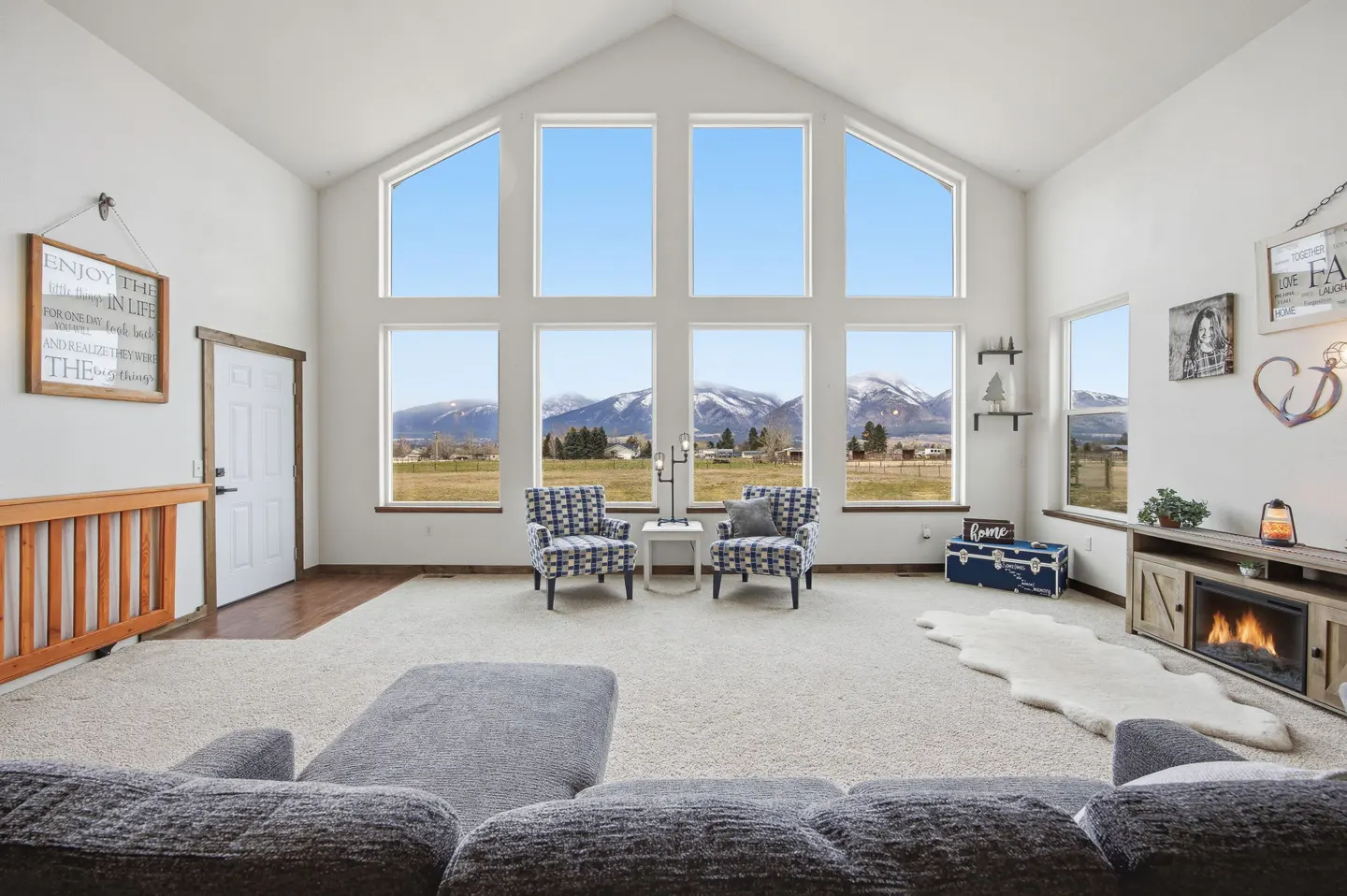 Bright living room with vaulted ceiling, large windows showing mountain view, two patterned chairs, and a gray sofa.