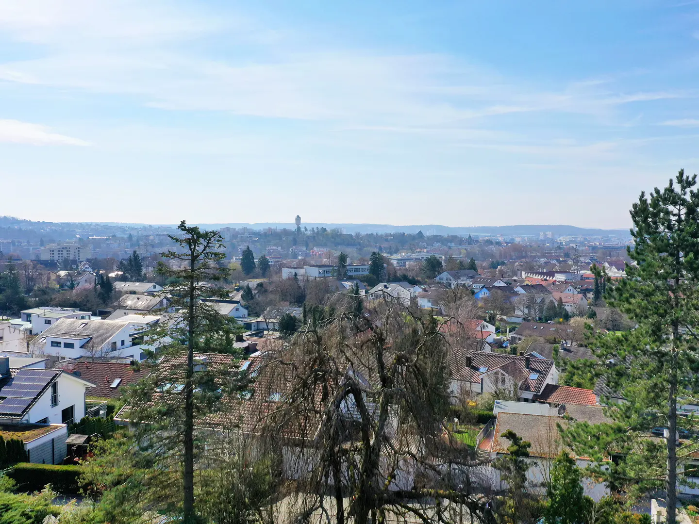View of a town with houses, trees, and a water tower in the distance under a blue sky.