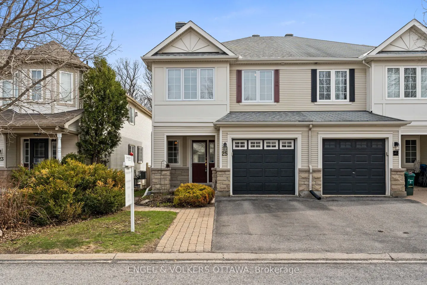 Two-story townhouse with beige siding, a dark garage door, and a brick walkway leading to the front door.