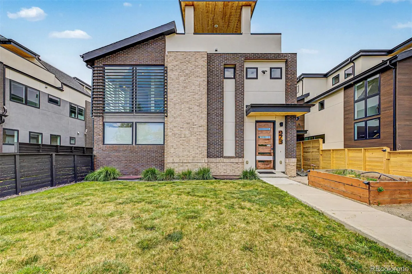 Modern two-story house with brick and beige siding, a wood door, and a green lawn.