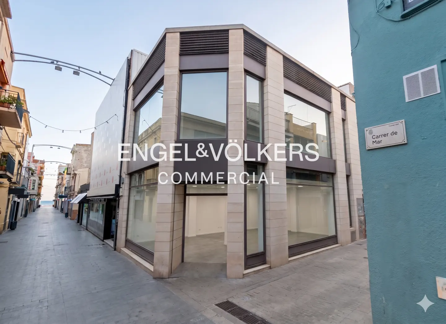 Engel & Völkers commercial property on a street corner with large windows. A blue building is on the right with a street sign.