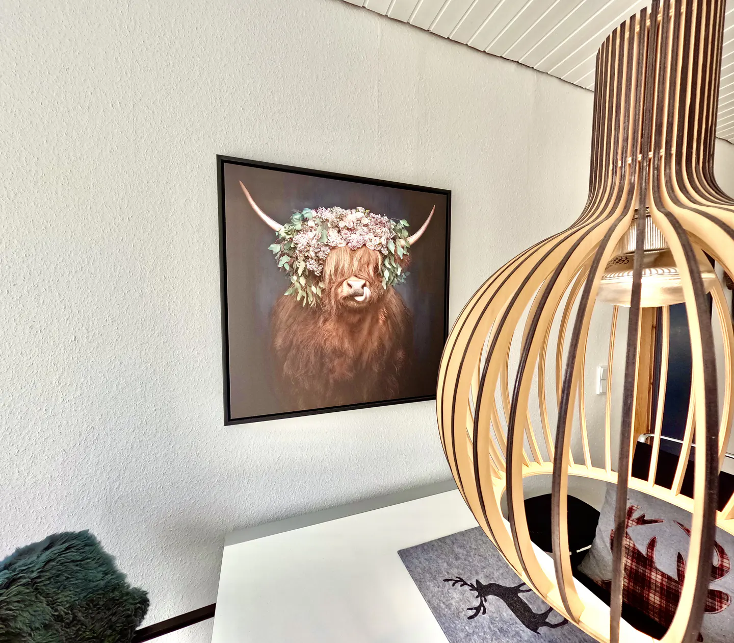 Interior view with a framed Highland cow print wearing a floral crown, and a modern wooden pendant light fixture.