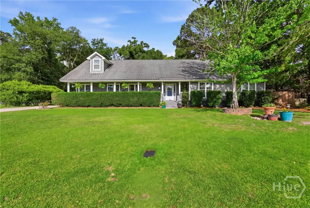 Gray ranch-style house with a dormer window, white trim, and a green lawn. A trimmed hedge runs along the front porch.