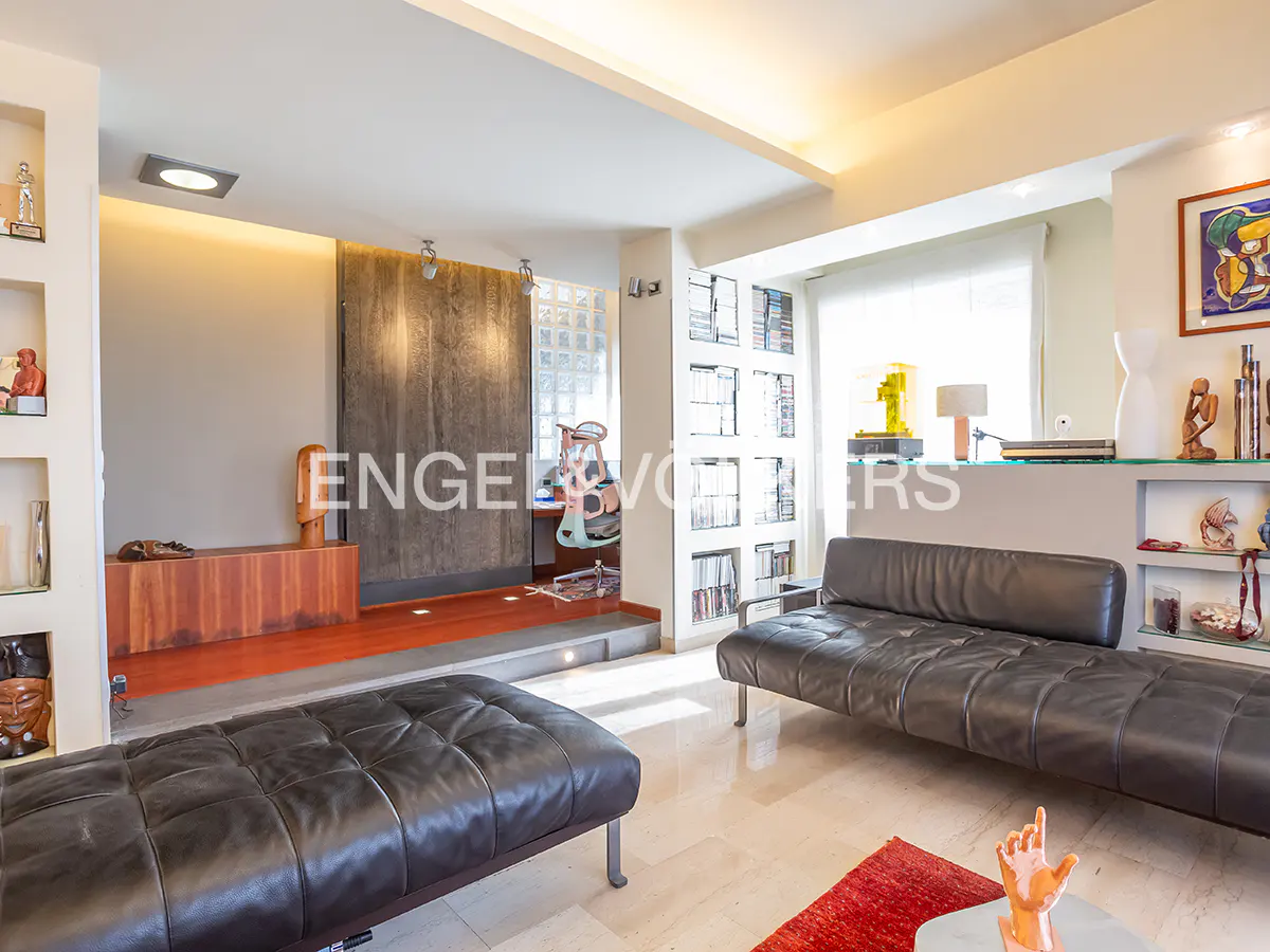 Living room with black leather sofas, marble floors, and built-in shelves. A desk area is visible in the background.