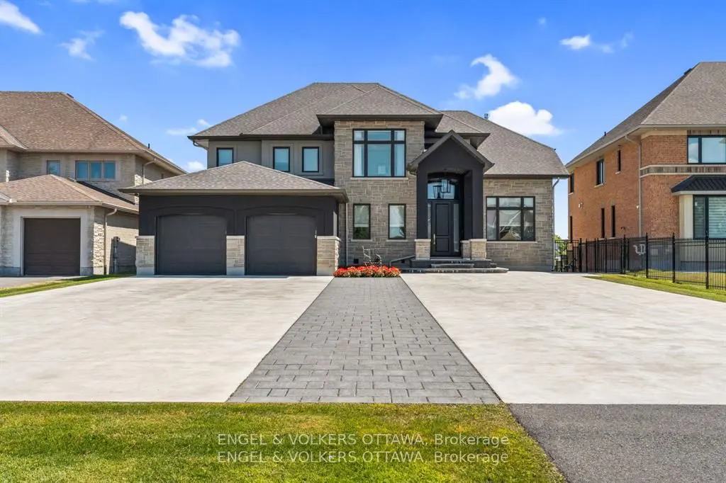 Two-story stone house with a gray roof, black trim, and a two-car garage on a sunny day.