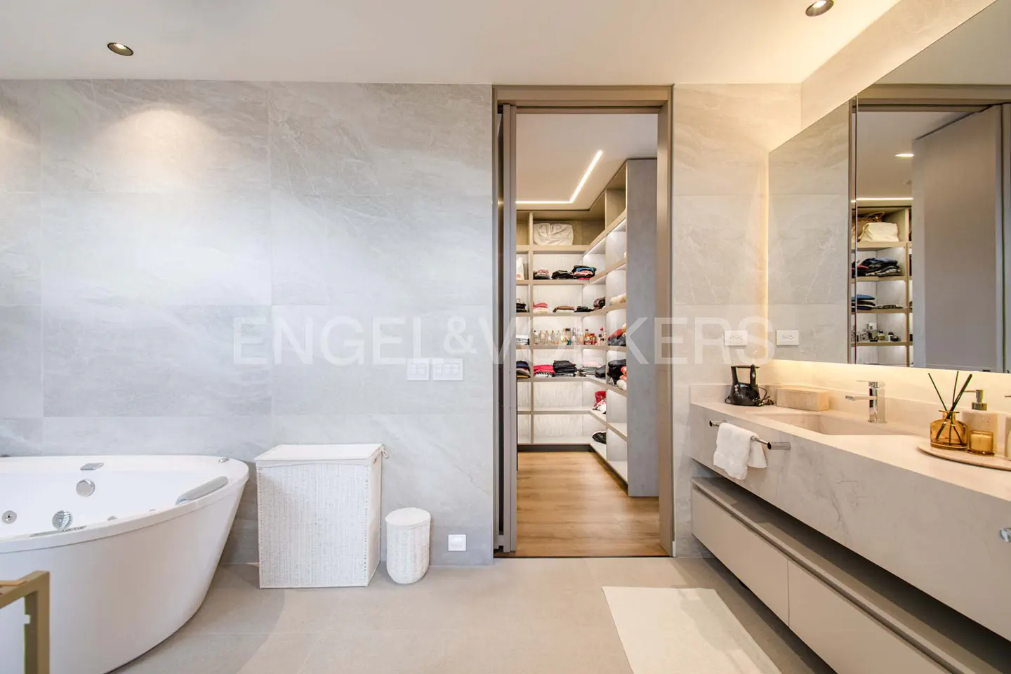 Bright bathroom with a white jacuzzi tub, a sink with a mirror, and an open door to a walk-in closet with shelves.