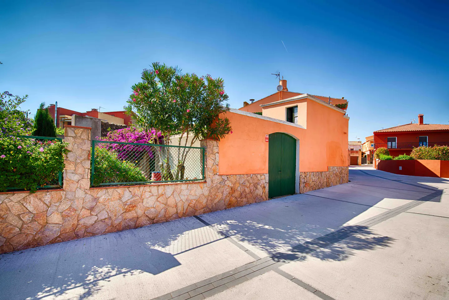 Exterior of an orange house with a green door and a stone wall with flowers on a sunny day.