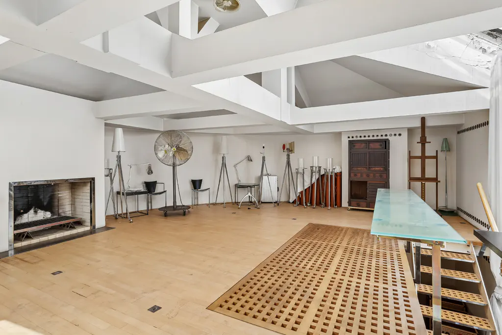 Bright, airy room with white walls, light wood floors, and a unique ceiling design. Features a fireplace, vintage fan, and art supplies.