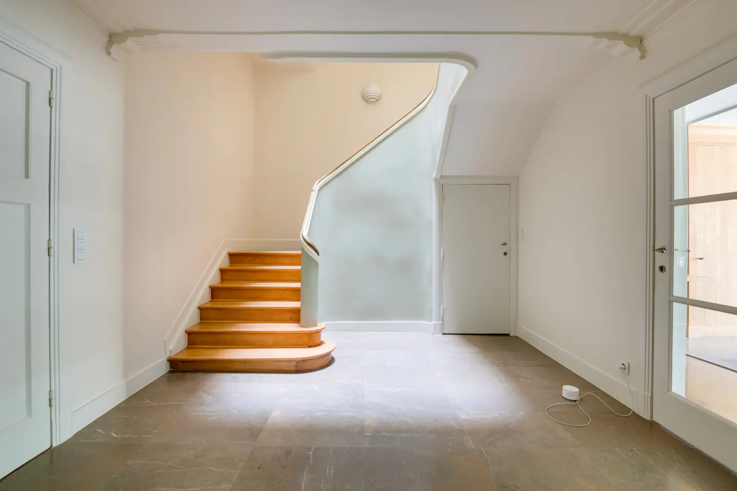 Bright foyer with wooden stairs, white walls, and gray tiled floor. A white door is on the left, and a glass-paneled door is on the right.