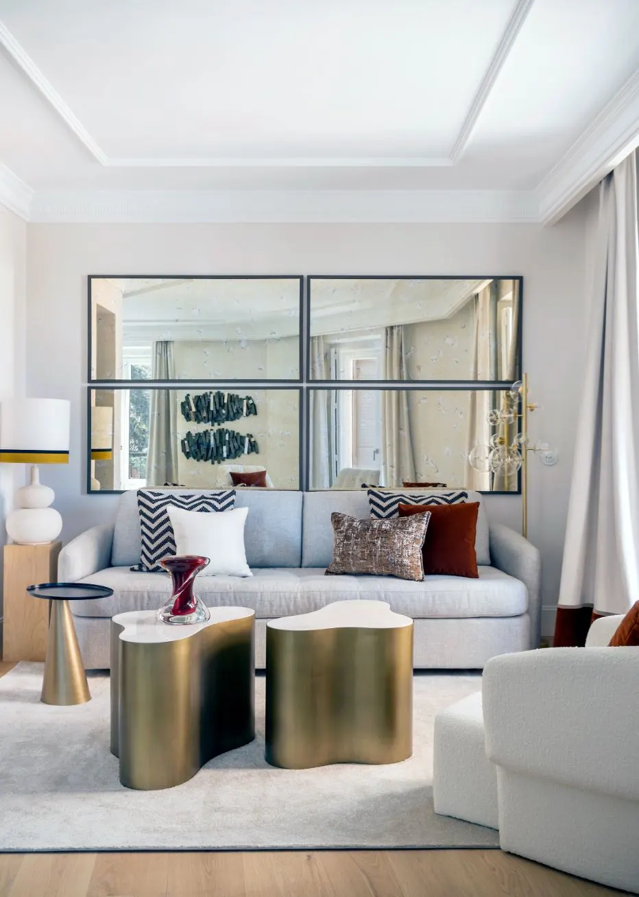 Modern living room with a long grey sofa, two gold organic-shaped coffee tables, and large rectangular wall mirrors.