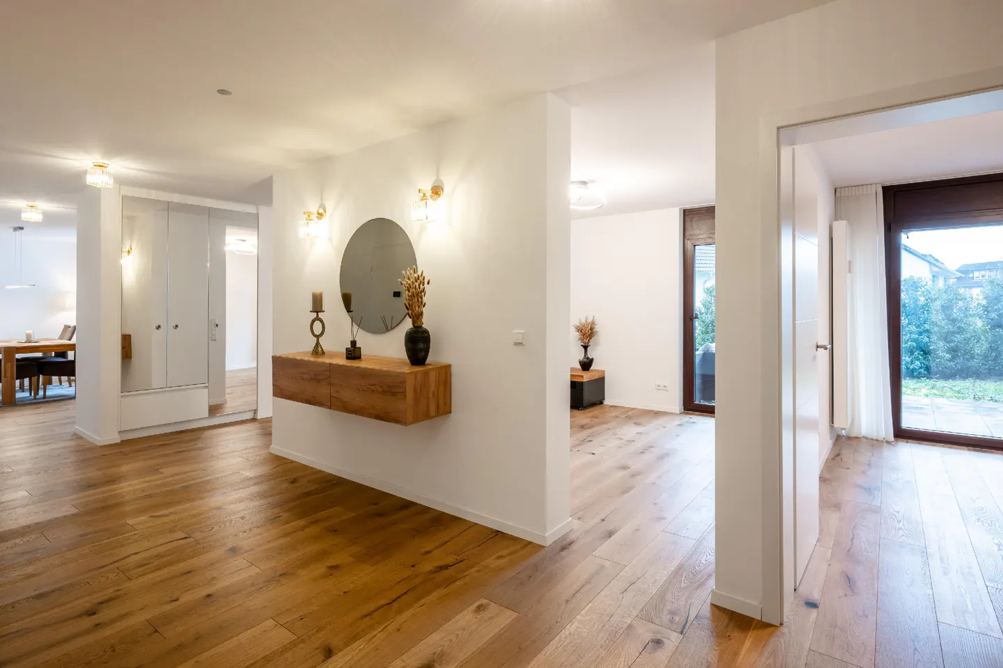 A bright hallway with wood floors, white walls, and a floating wood console table with a round mirror above it.