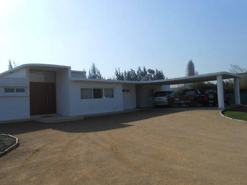 A modern, white, one-story house with a carport and several cars parked in the driveway.