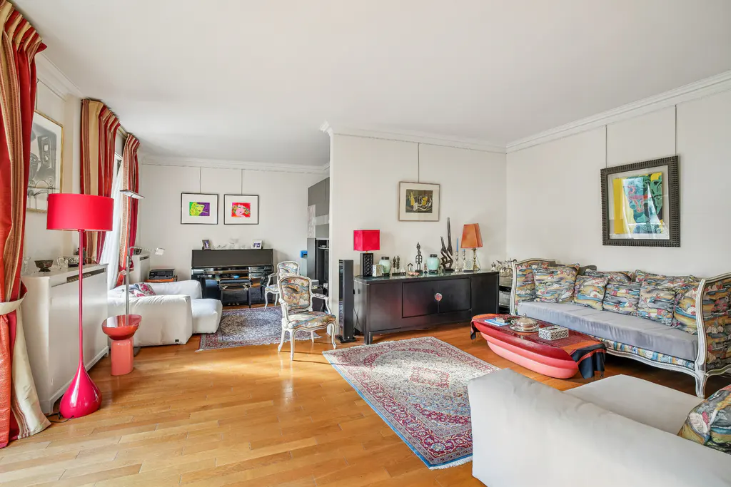 Bright living room with hardwood floors, white sofas, and colorful accents. Red floor lamp and coffee table add pops of color. Art adorns the walls.