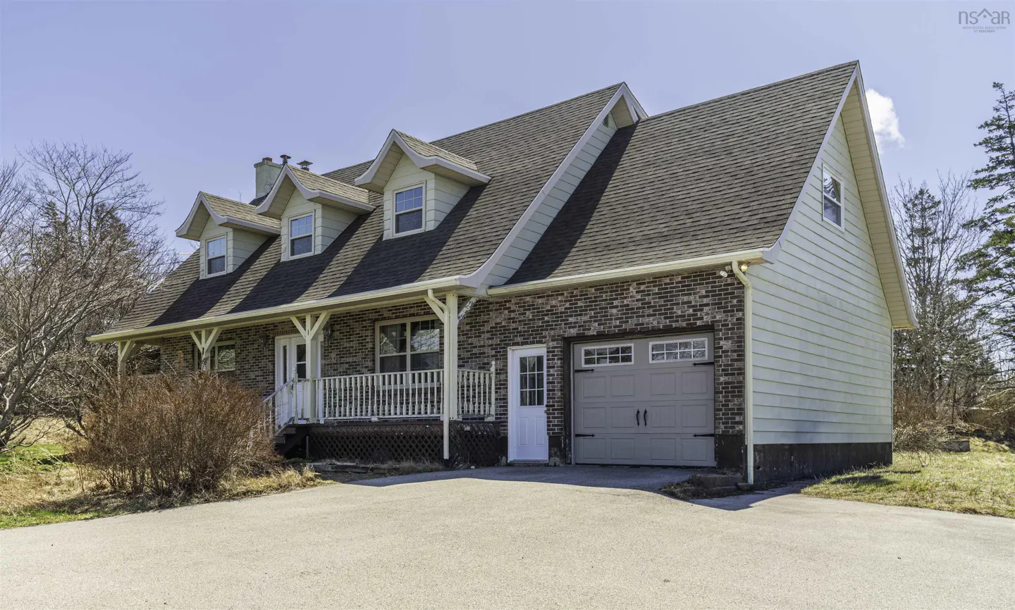 A brick and siding house with a gray garage door and a white porch railing.