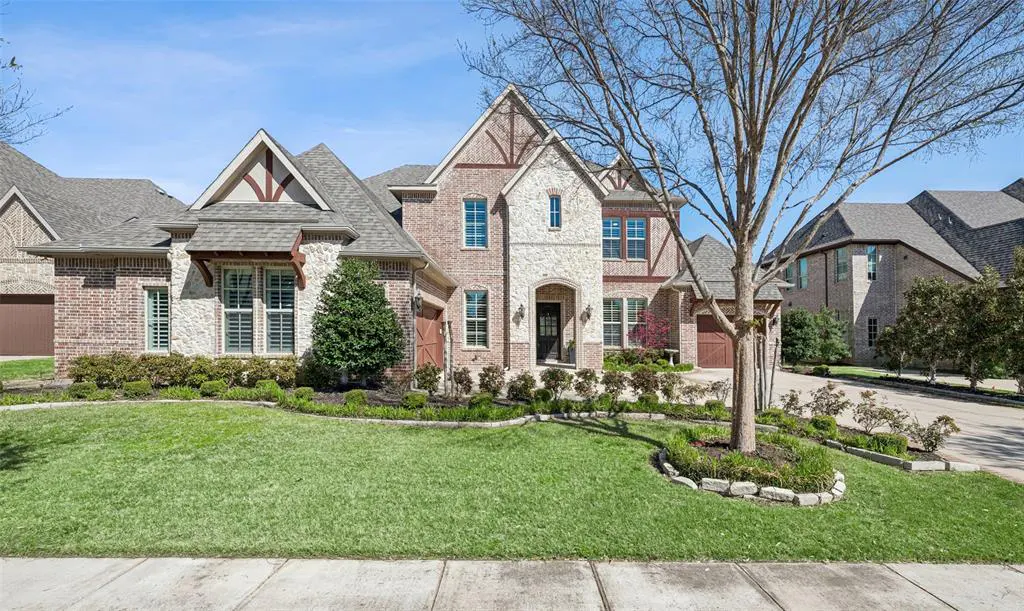 Two-story brick and stone house with a manicured lawn and landscaping under a blue sky.
