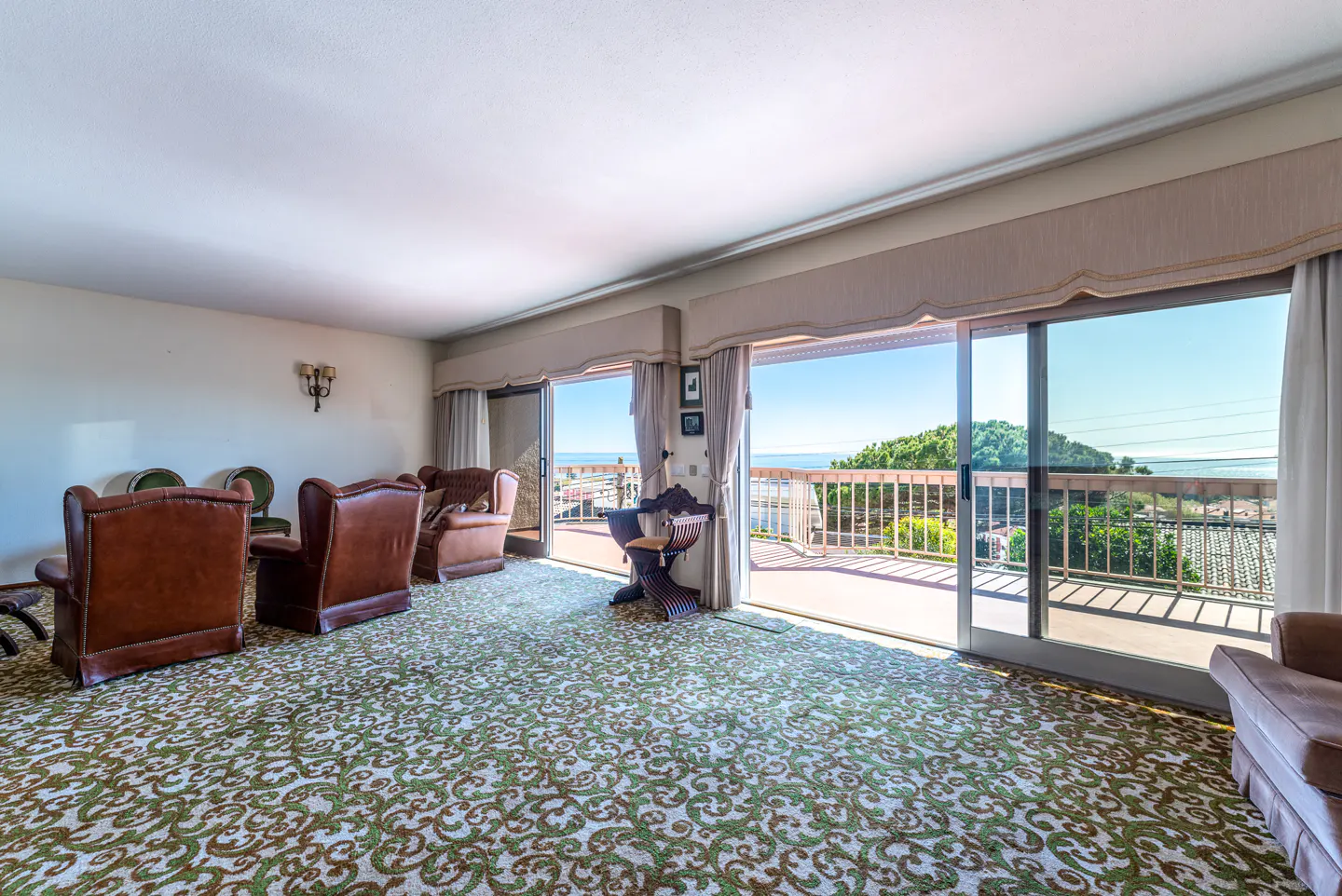 Living room with brown leather chairs, green patterned carpet, and sliding glass doors to a balcony with ocean views.
