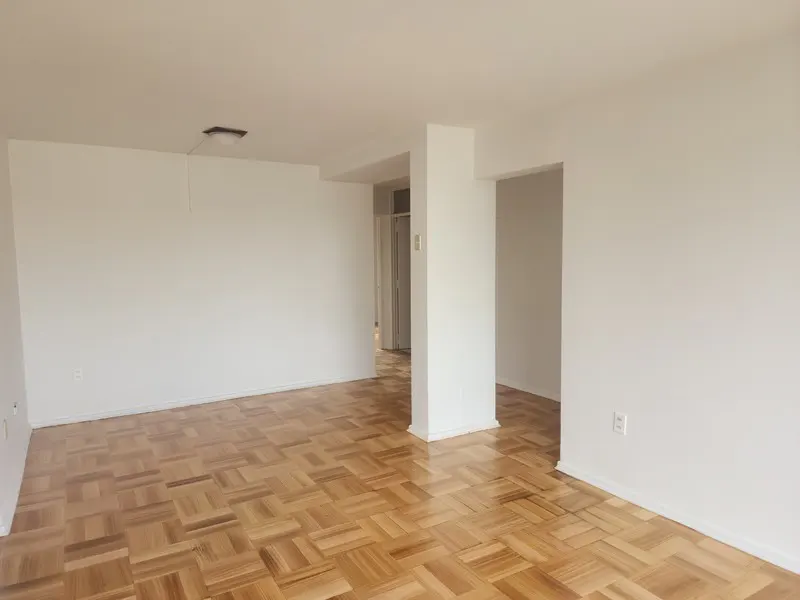 Empty room with white walls, light wood parquet flooring, and an open doorway leading to a hallway.