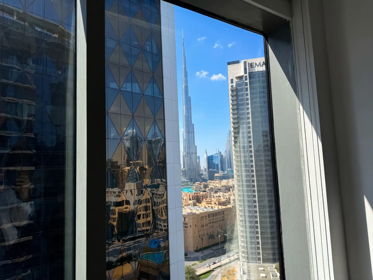 View from a window of Dubai's skyline, featuring the Burj Khalifa and other skyscrapers under a blue sky.