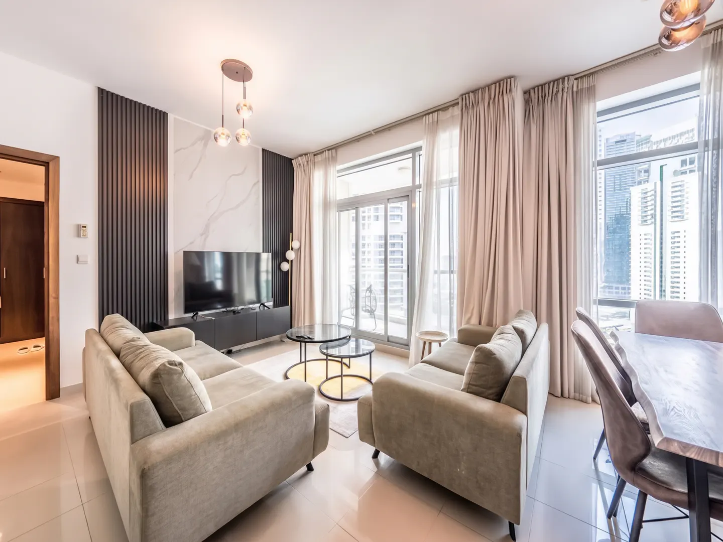 A modern living room with beige sofas, glass tables, and a TV, with city views through large windows.