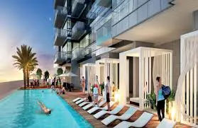 Condo building with a pool, lounge chairs, and cabanas. People are swimming and relaxing by the pool.