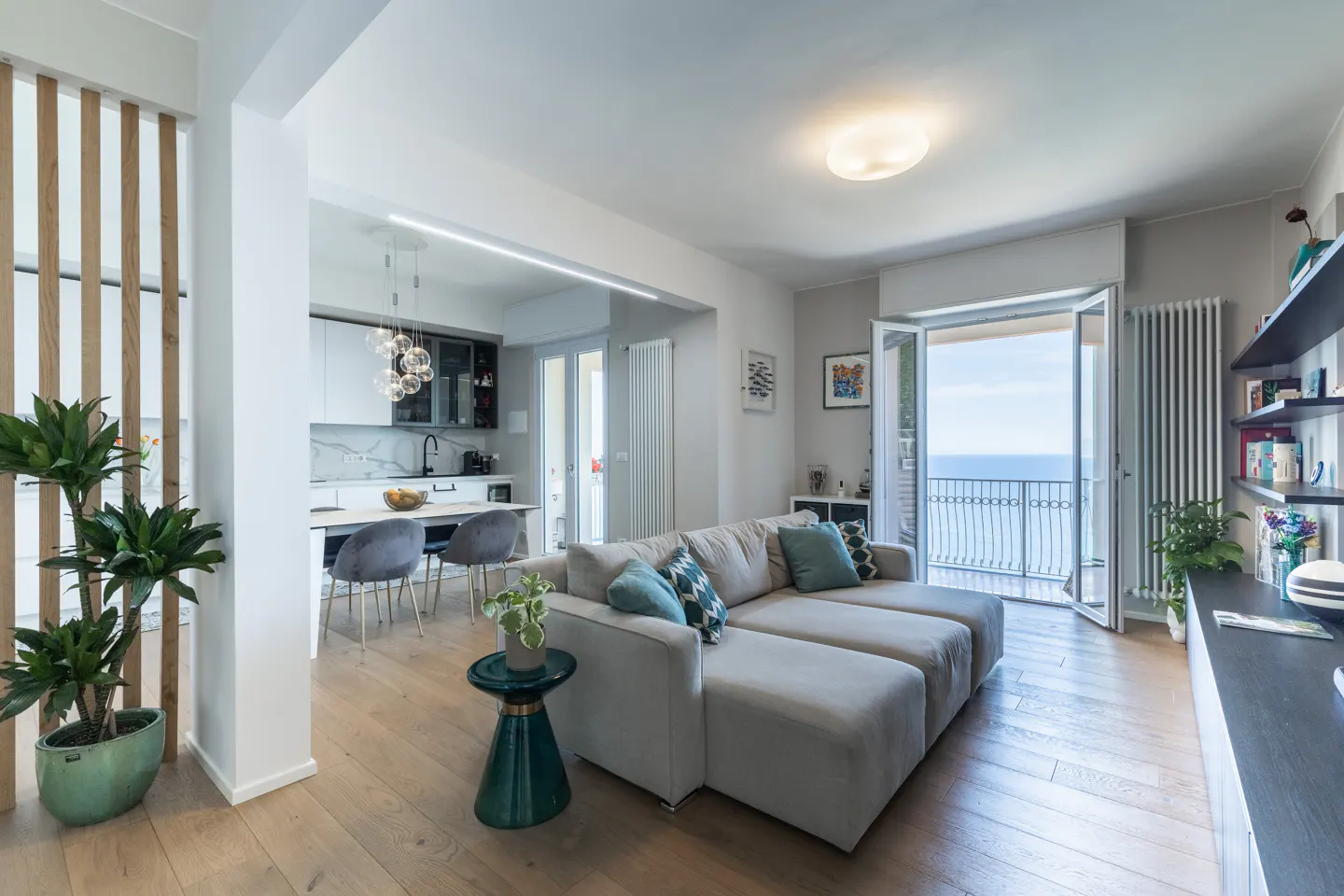 Bright, open-concept living space with a gray sectional sofa, wood floors, and a view of the ocean from the balcony.