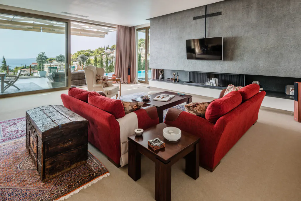 A modern living room with red sofas, a gray accent wall with a TV, and a view of a pool and ocean through large windows.