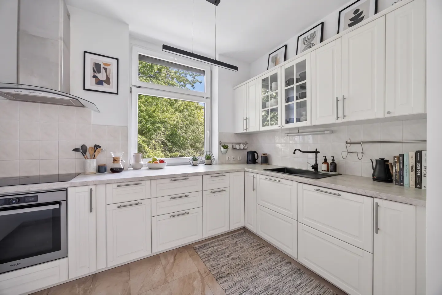 Bright kitchen with white cabinets, marble countertops, and a black sink. A window overlooks green trees.