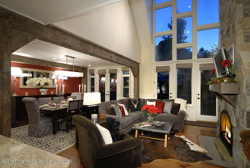 Living room with stone fireplace, gray sectional sofa, and dining area with red wall. Large windows offer a view of the night sky.