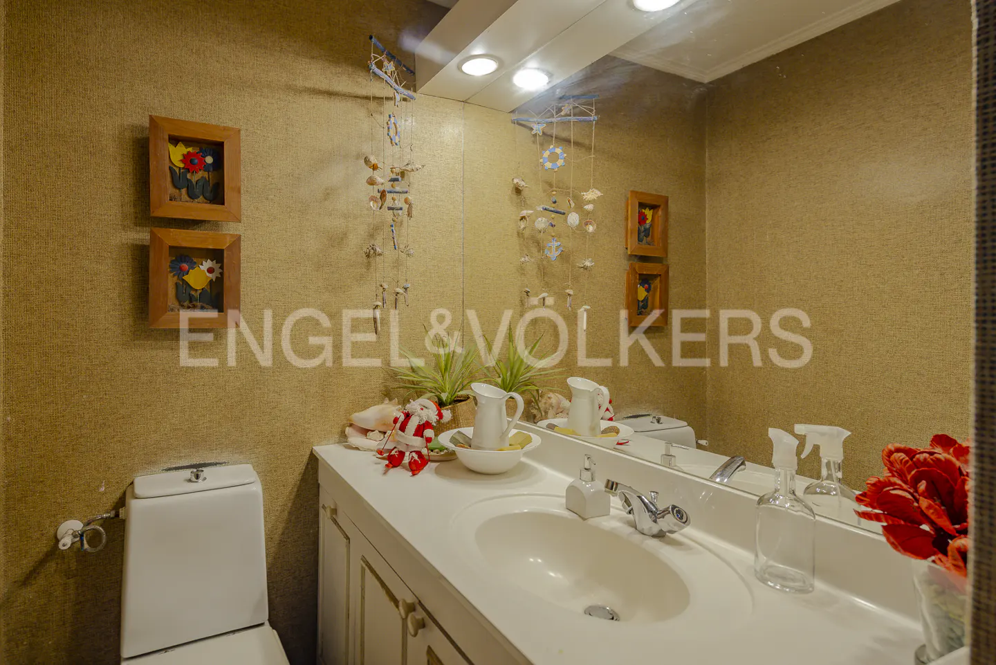 Bathroom with tan walls, white vanity, sink, toilet, hanging shell decor, and festive Christmas accents.