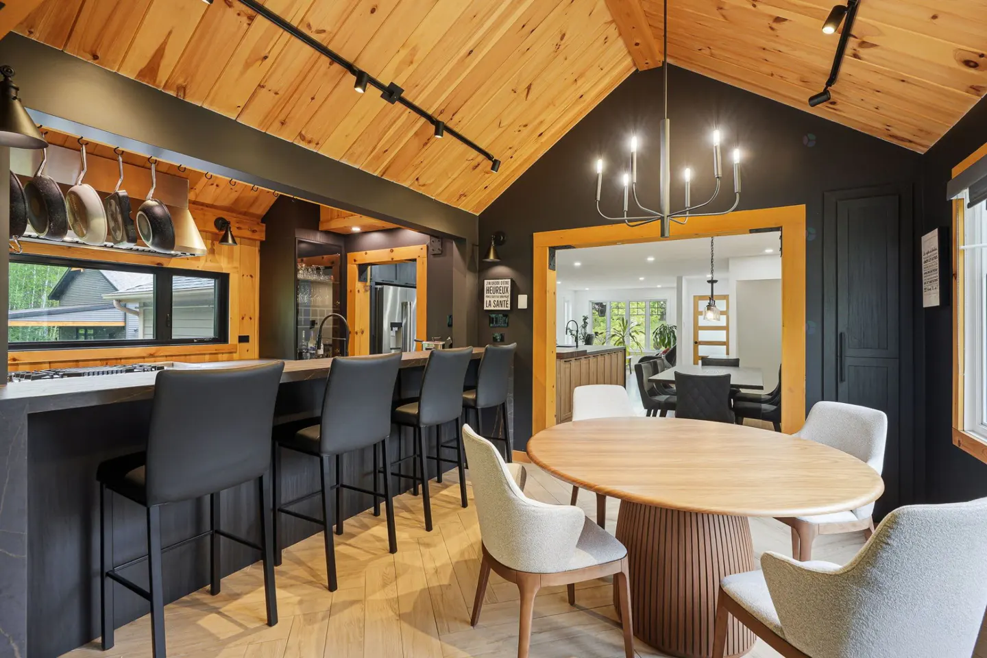 Modern kitchen with black cabinets, wood-paneled vaulted ceiling, breakfast bar with stools, and a round dining table.