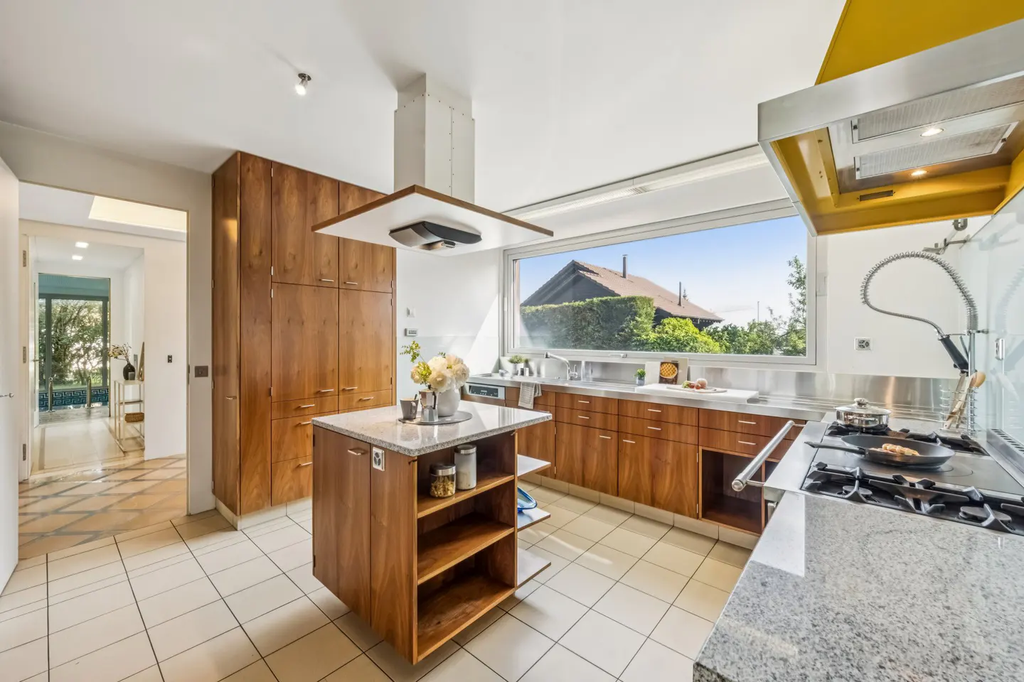 A bright kitchen with wood cabinets, a granite island, and a large window overlooking a green yard.