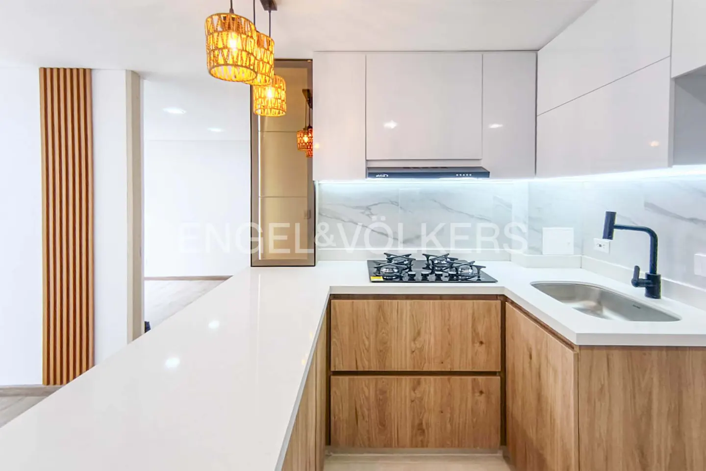 A modern kitchen with white cabinets, wood-grain lower cabinets, a white countertop, and woven pendant lights.
