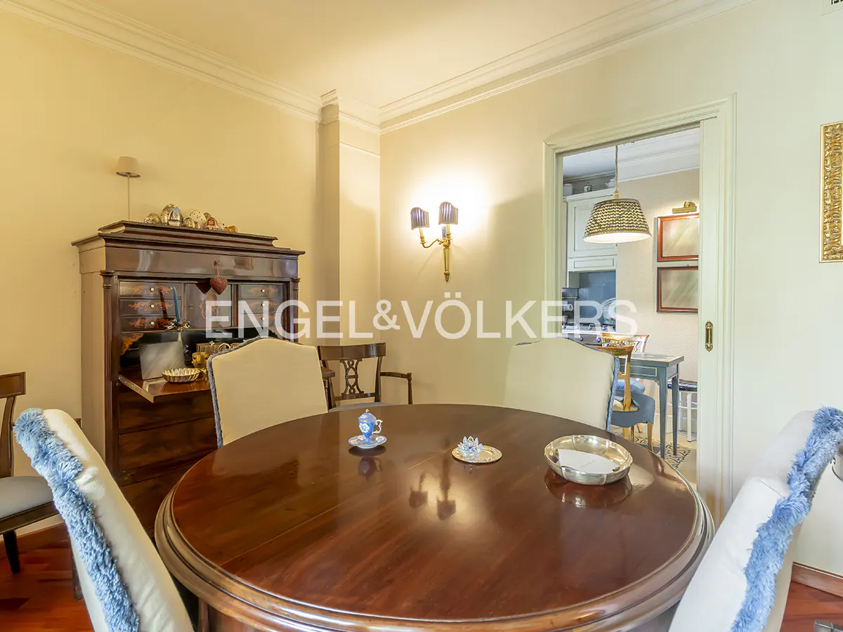 Dining room with a round wooden table, cream chairs with blue trim, and a dark wood secretary desk.