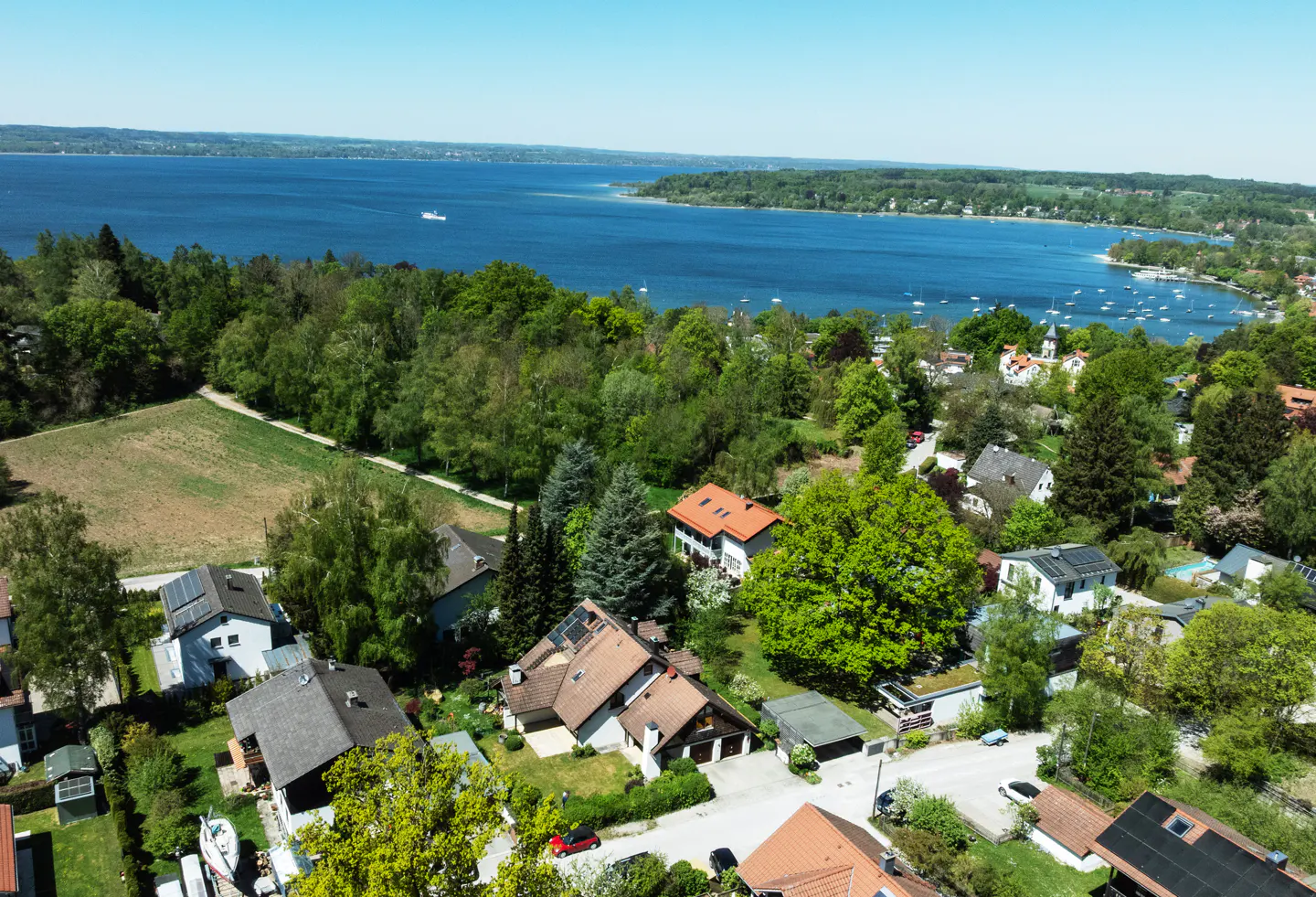 Aerial view of houses with red roofs near a blue lake and green trees on a sunny day.