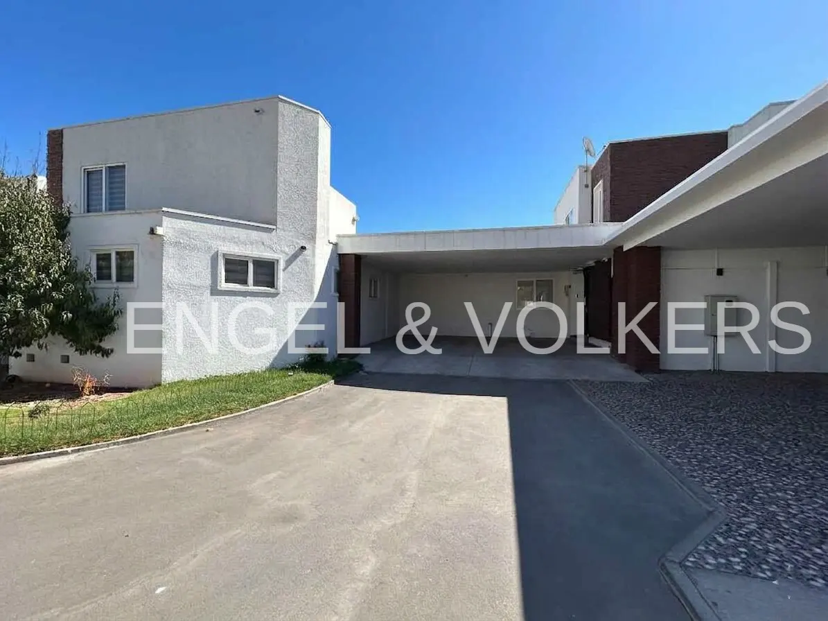 Exterior of a modern white house with a covered parking area and the Engel & Volkers logo. Blue sky is visible.