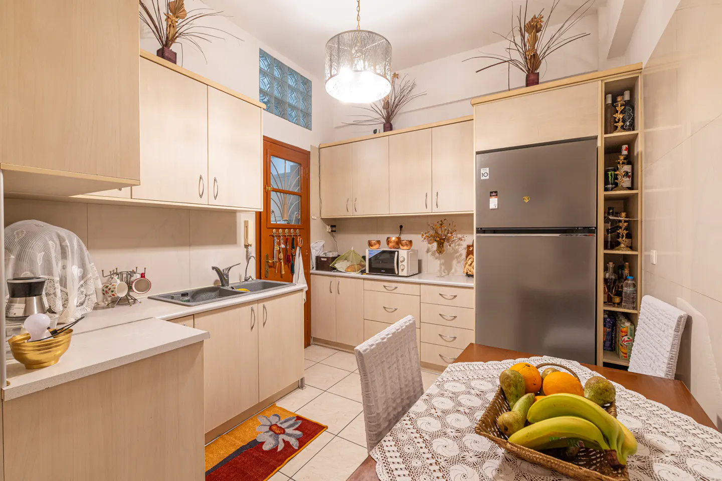 Bright kitchen with light wood cabinets, stainless steel fridge, and a table with fruit basket.