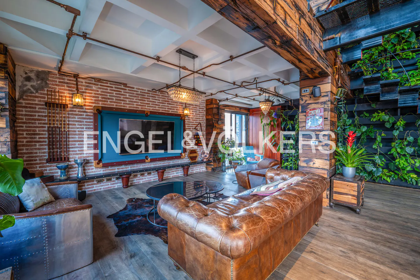 Living room with a brown leather sofa, brick wall, and a TV framed like a pool table. Plants and wooden beams add to the rustic design.