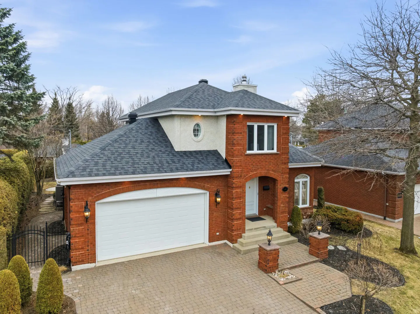 Two-story red brick house with a gray roof, white garage door, and a brick driveway.