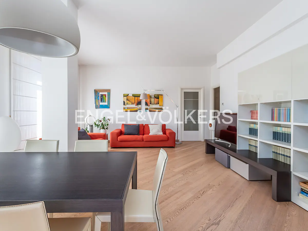Bright living room with a dark dining table, red sofa, white shelving unit, and light wood floors.