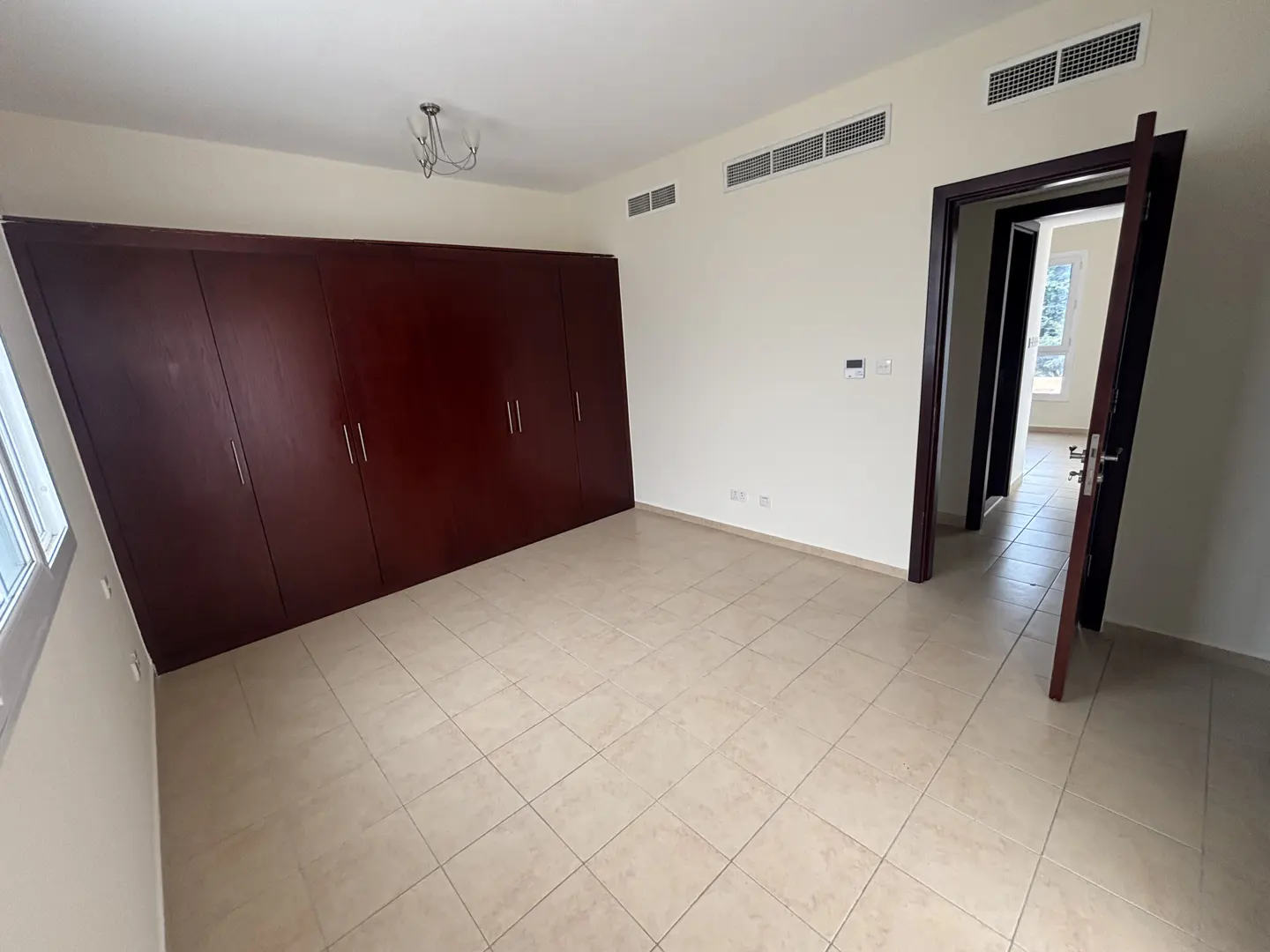 A bedroom with beige tile flooring, cream walls, and a large, dark wood closet. An open doorway leads to another room.