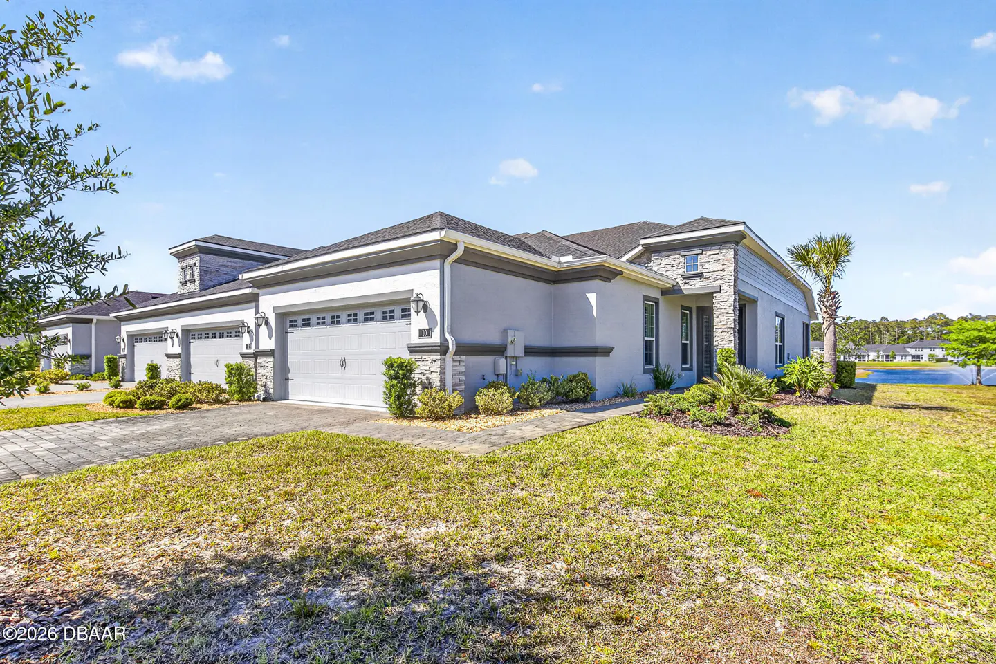 Exterior view of a light gray, single-story home with a two-car garage and stone accents. Green lawn and blue sky.