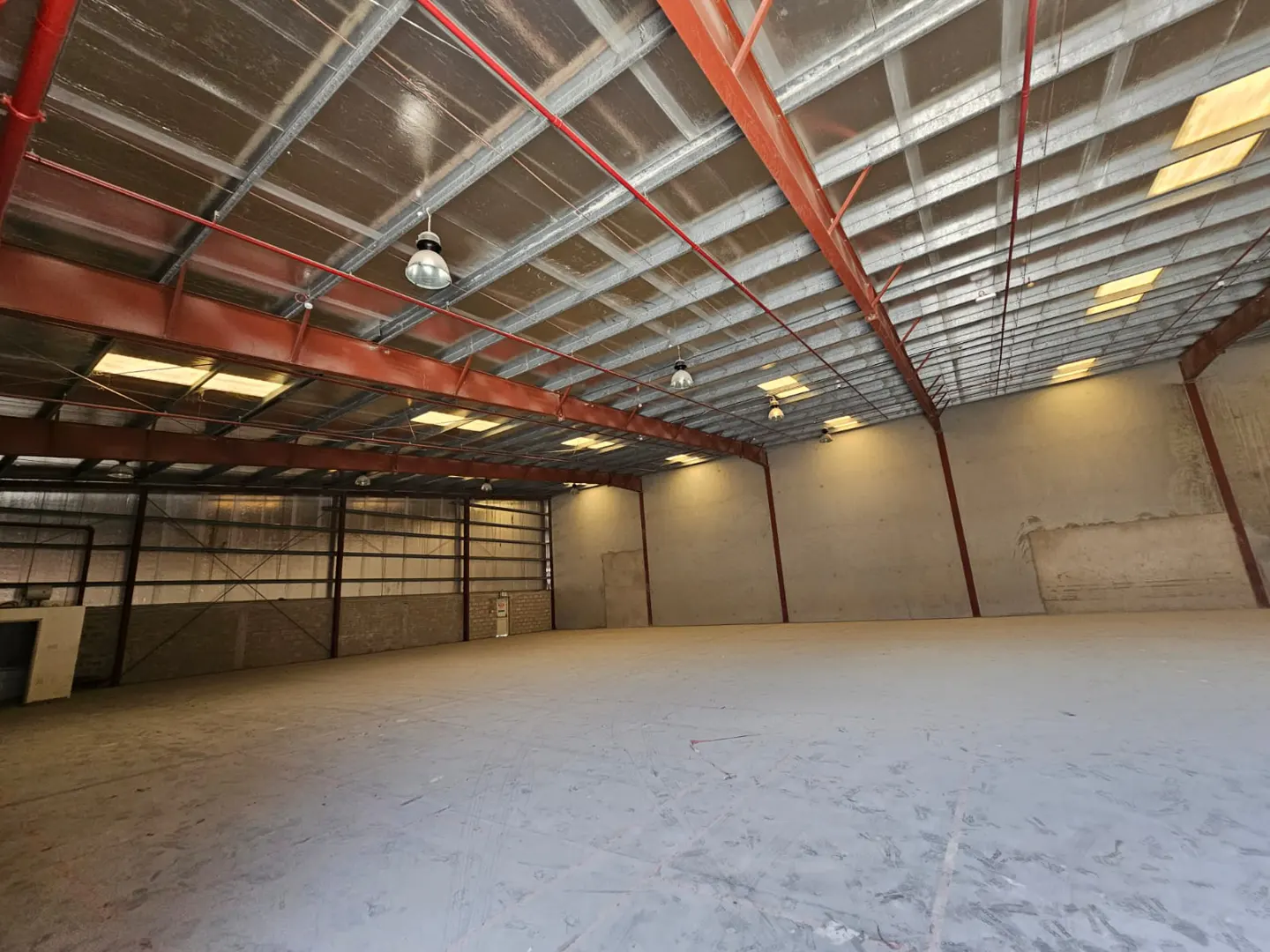 A large, empty warehouse with a concrete floor, metal beams, and overhead lighting.