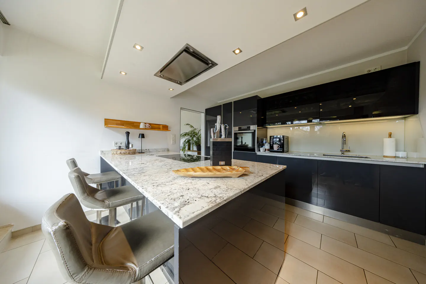 Modern kitchen with a granite island, black cabinets, and three gray bar stools. A wooden tray sits on the island.