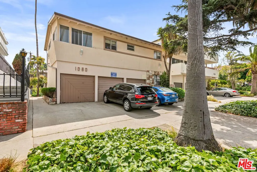 A two-story tan apartment building with brown garage doors and two parked cars.